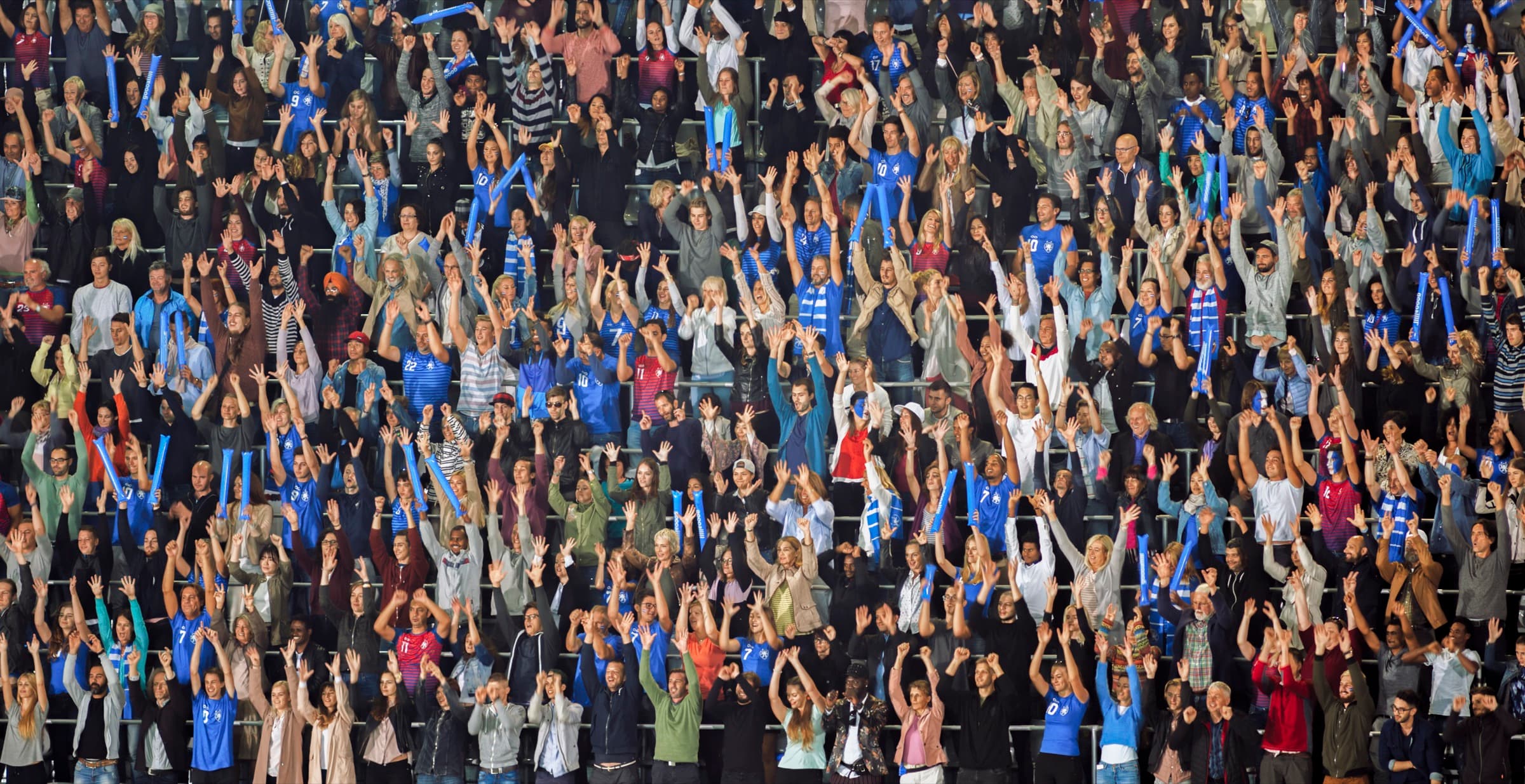 A packed stand of supporters in blue with their arms raised